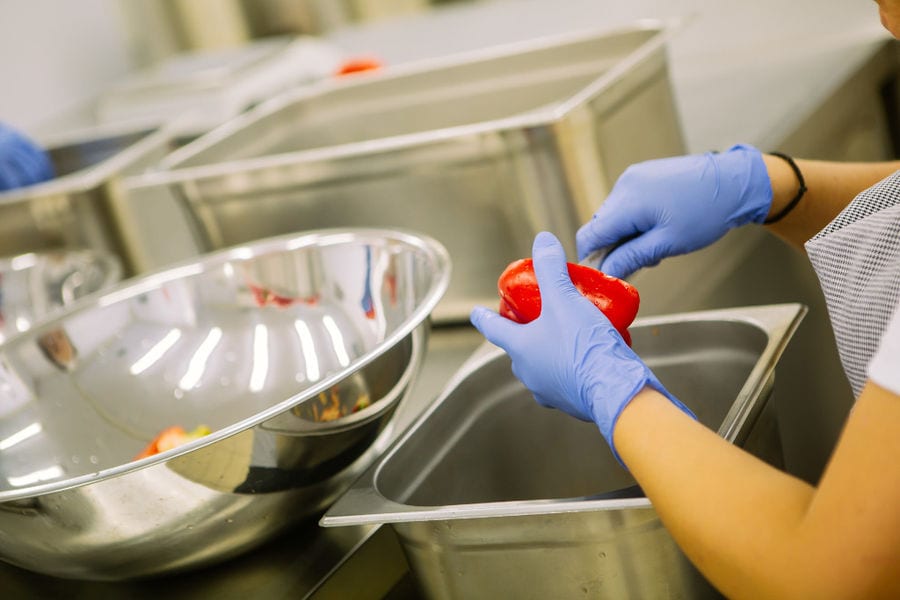 a woman wearing plastic gloves cutting a red 'Florina' pepper with a knife on the aluminum buscket at 'Rizes' plant